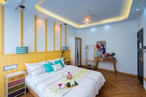 Un dormitorio con cama, mesitas de noche, cómoda, lámpara y un cuadro en la pared.