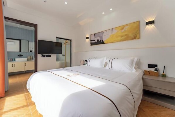 A modern hotel room with a large bed, a flat-screen TV, a painting on the wall, and a bathroom visible through an open door. - Slow Life Theme Inn (Suzhou)