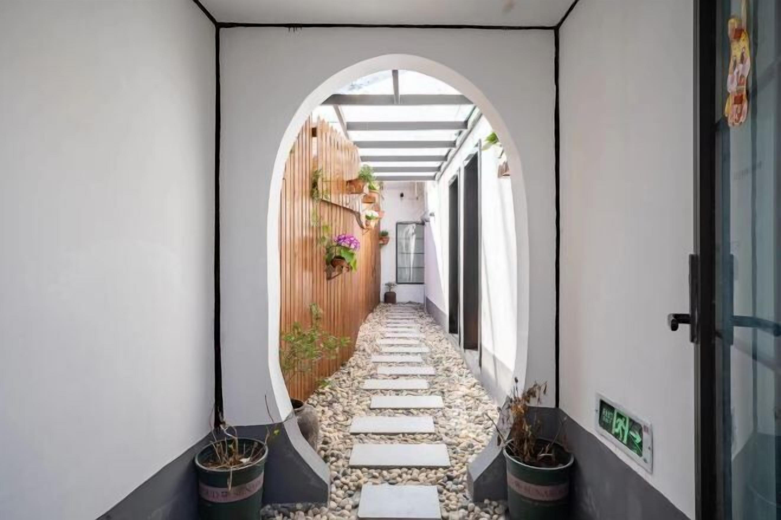 A narrow hallway with a wooden wall, potted plants, and a stone pathway leading to a door.