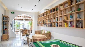 Une pièce bien éclairée, avec une table de billard verte, une bibliothèque en bois remplie de livres et un coin salon confortable avec un canapé et des fauteuils.