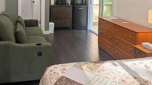 A bedroom with a green sofa, a wooden dresser, a microwave, and a bed with a floral quilt. - Cute Cabin Nested in Pine Trees_Cabin 12A (Bar Harbor)