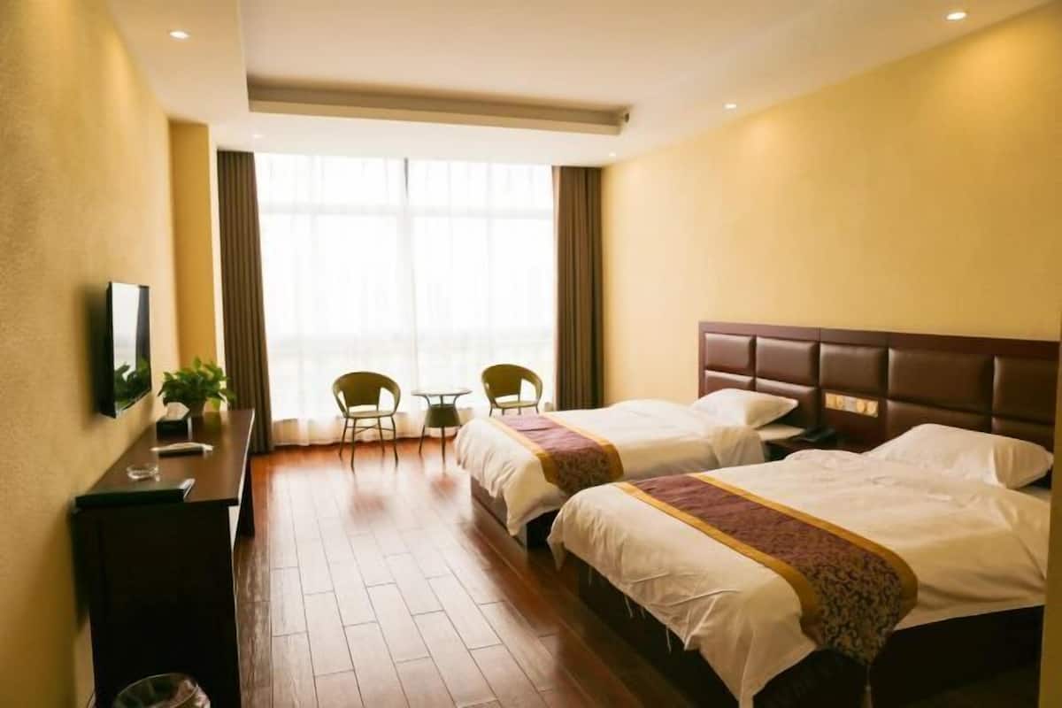 Une chambre d’hôtel avec deux lits, un bureau, une chaise et une fenêtre avec des rideaux.