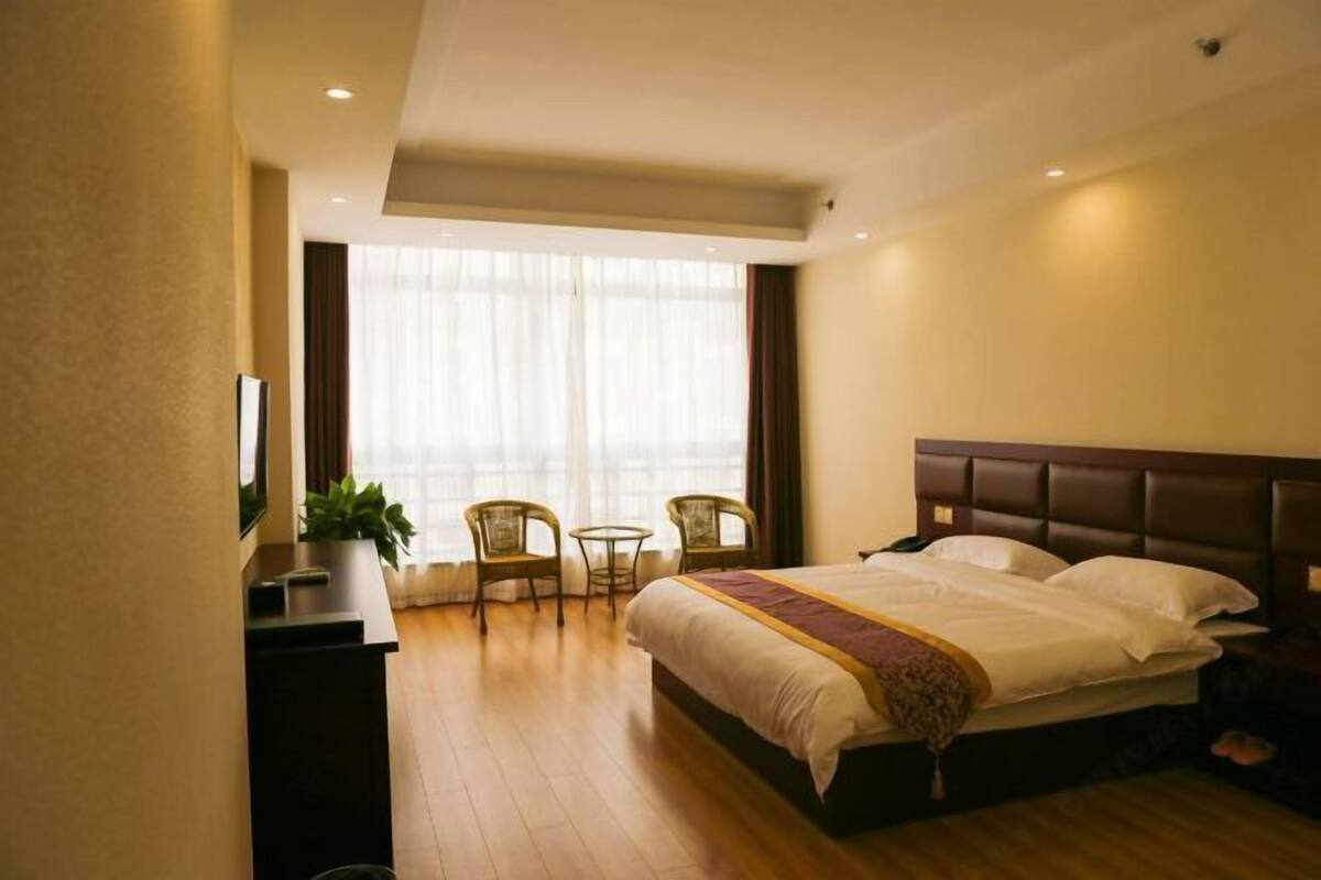 Une chambre d’hôtel avec un lit, un bureau, une chaise, une petite table et une fenêtre avec des rideaux.