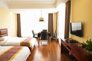 Een hotelkamer met twee bedden, een eettafel met stoelen, een televisie en een plant.