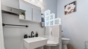 A modern bathroom with a white sink, black faucet, and a toilet. There is a mirror above the sink, a towel rack, and a framed picture on the wall. - Stylish Studio Suite Near Downtown Anchorage - Explore Alaska's Beauty with Ease (Anchorage)