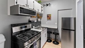 A compact kitchen with a gas stove, microwave, stainless steel refrigerator, and a small bar area with stools. - Stylish Studio Suite Near Downtown Anchorage - Explore Alaska's Beauty with Ease (Anchorage)