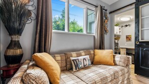 A cozy living room with a patterned sofa, a decorative vase, and a "Welcome" pillow. - Stylish Studio Suite Near Downtown Anchorage - Explore Alaska's Beauty with Ease (Anchorage)