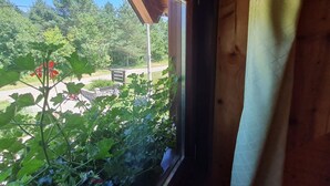A window with a view of a green landscape, a wooden structure, and a stone wall.