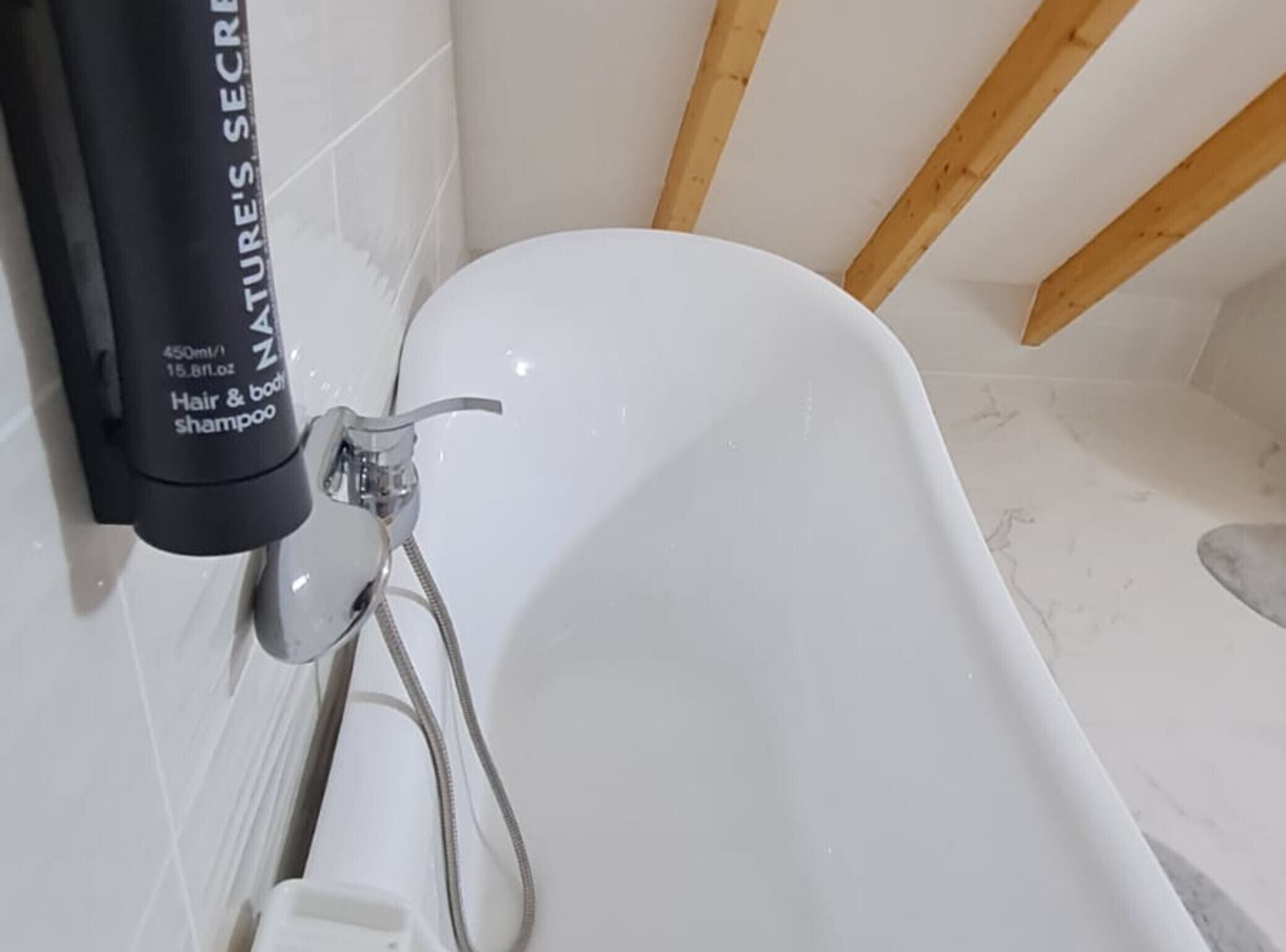 Et badeværelse med et hvidt badekar, brusearmatur og en shampoo.