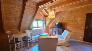 A cozy attic room with a dining table, chairs, a sofa, and a television.