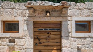 Ein rustikales Steinhaus mit einer Holztür, zwei Fenstern und einer kleinen Leuchte über der Tür.