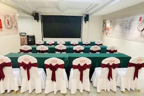 A conference room with tables and chairs, a projector screen, and a wall with artwork. - Xiangjiang International Hotel (Huai'an)