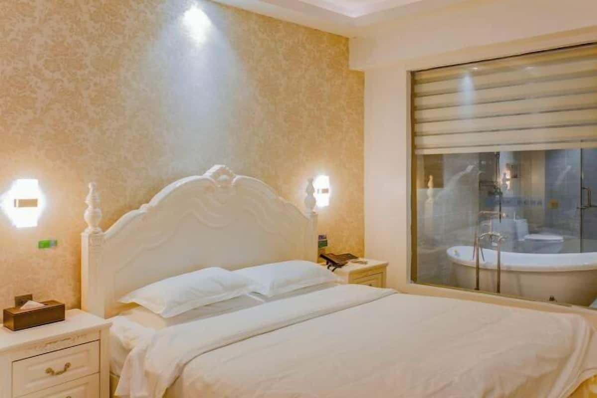 Une chambre d’hôtel avec un lit, une table de chevet, une lampe et une vue sur une salle de bain équipée d’une baignoire.
