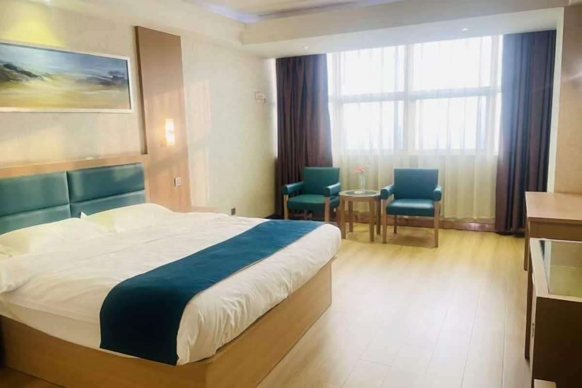 Une chambre d’hôtel avec un grand lit, un bureau, deux chaises, une petite table et une fenêtre avec des rideaux.