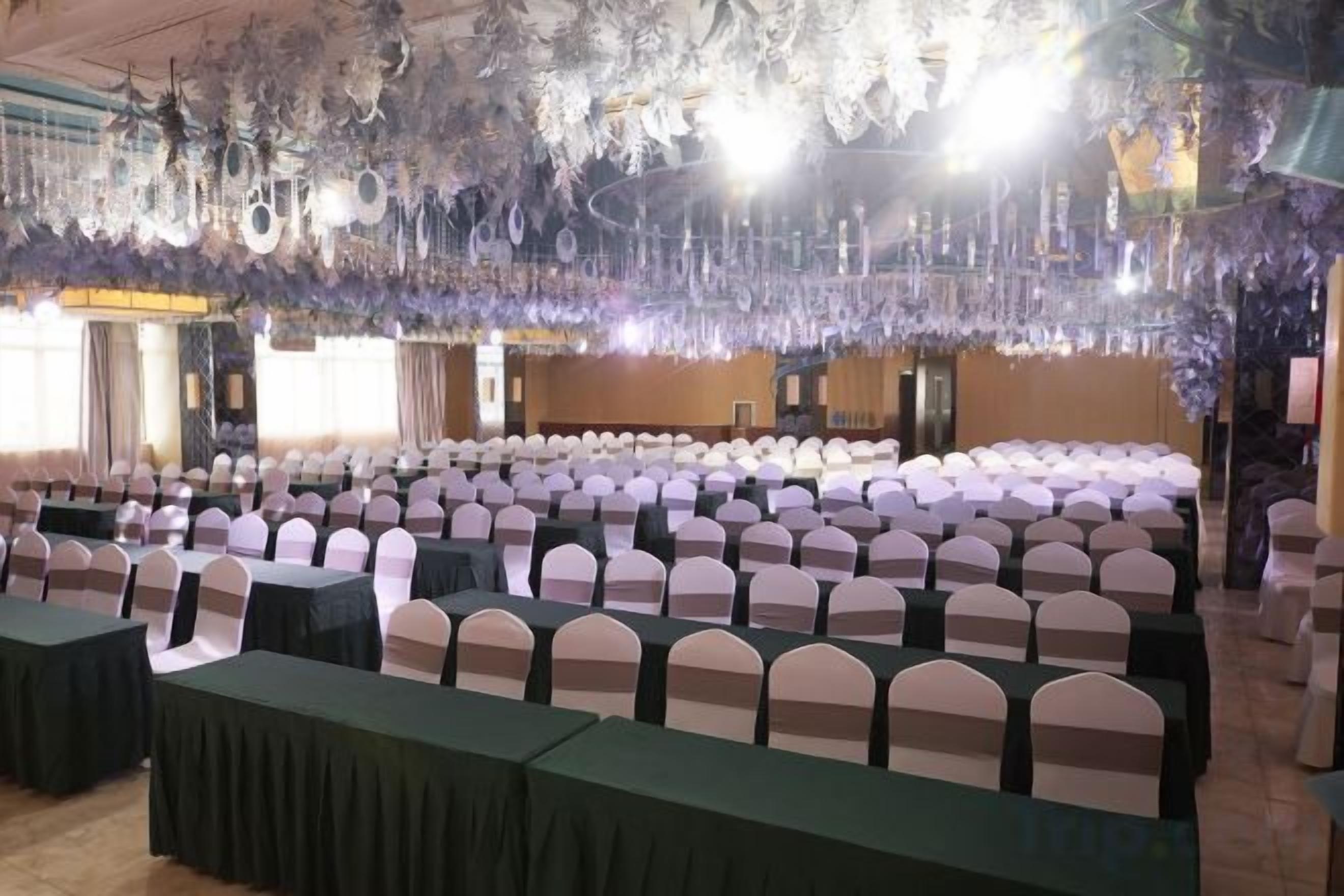 Una sala de banquet amb files de taules i cadires, un escenari amb un podi i una làmpada penjant.