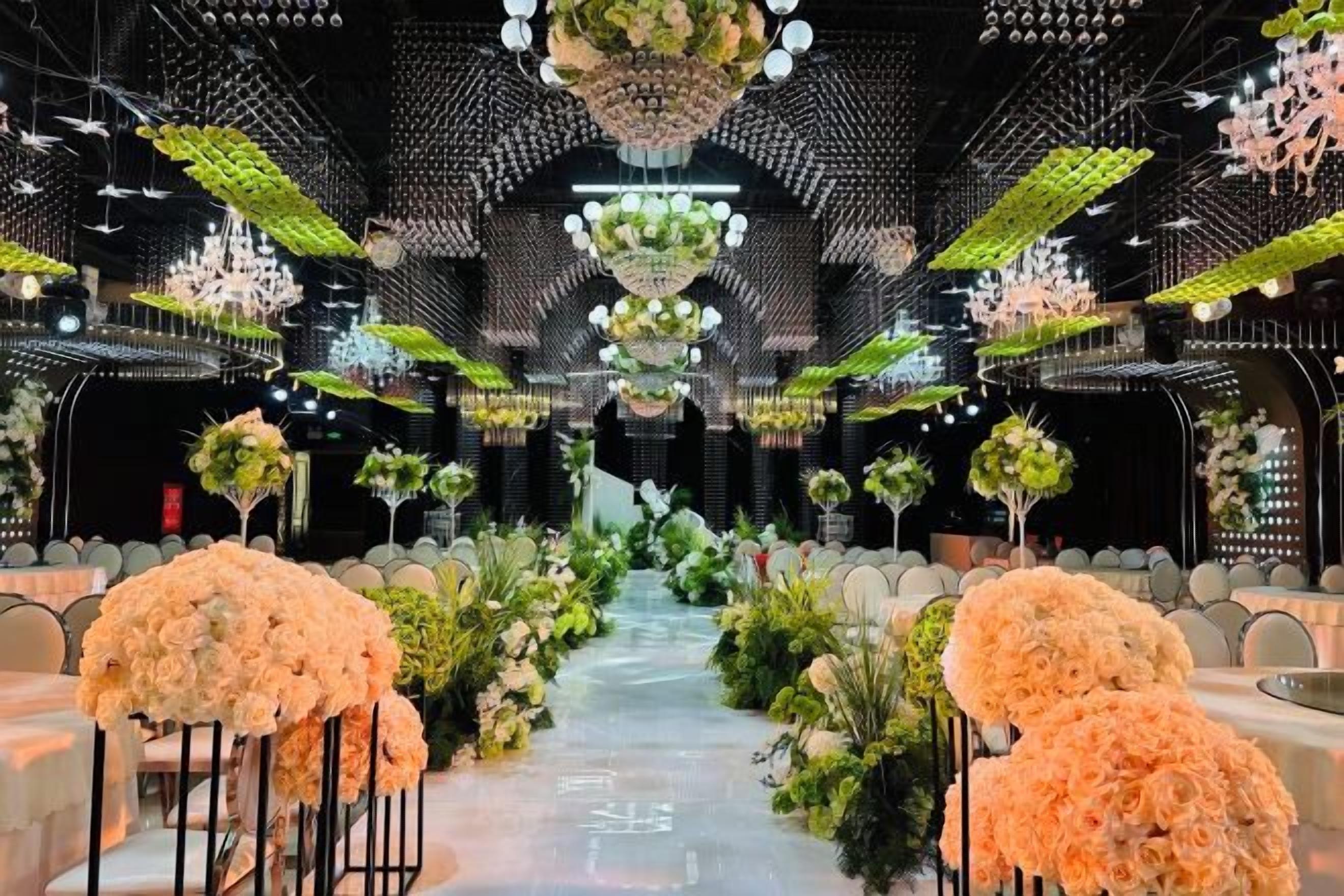 Un espace doté d’une allée centrale bordée de rangées de tables, chacune agrémentée de compositions florales et de chaises.