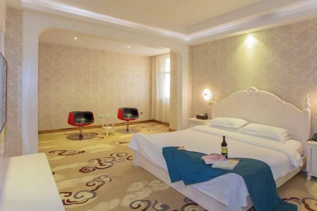 Une chambre d’hôtel avec un lit, une table de chevet, une lampe et deux chaises.