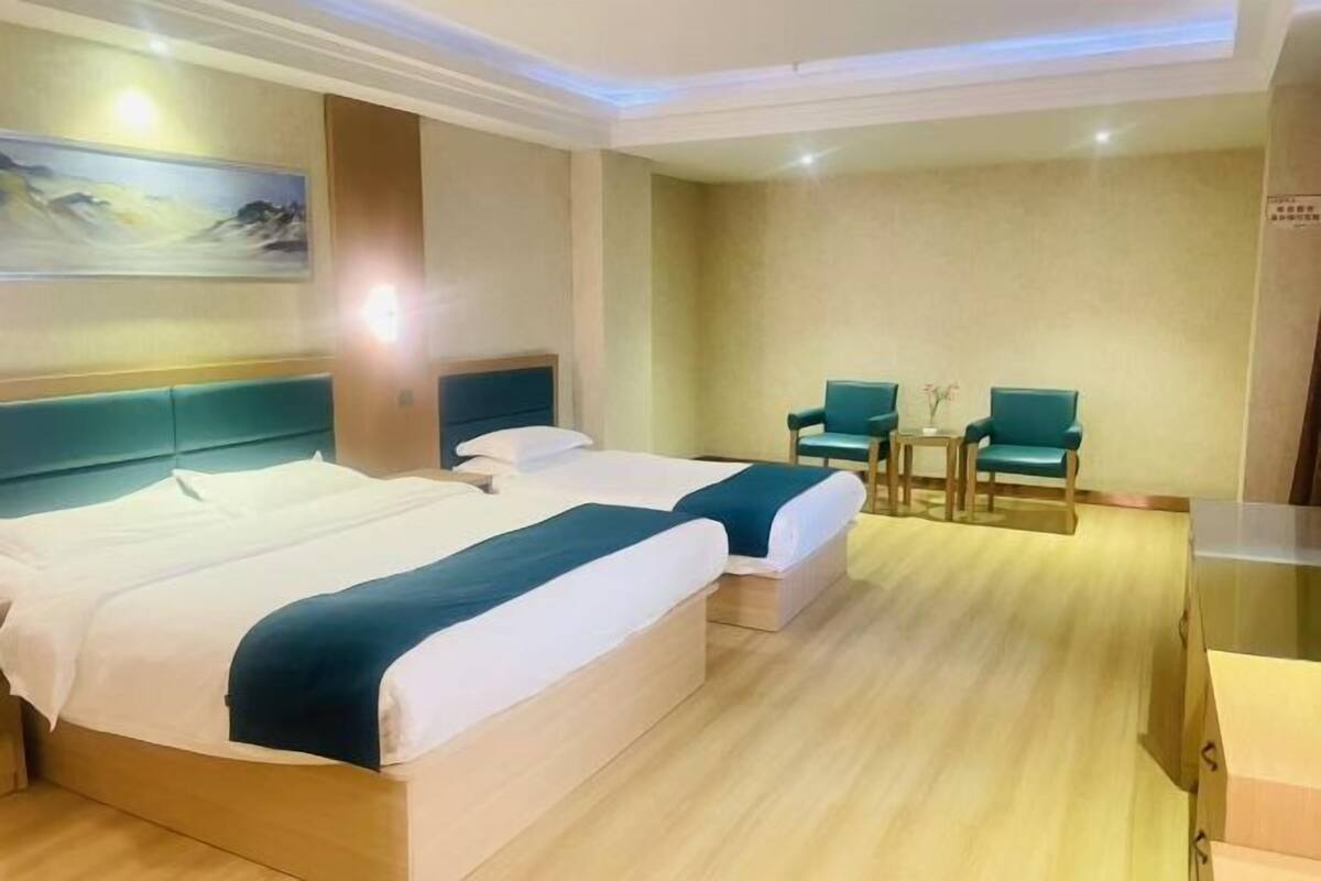 Une chambre d’hôtel avec deux lits, une petite table, deux chaises et un tableau au mur.