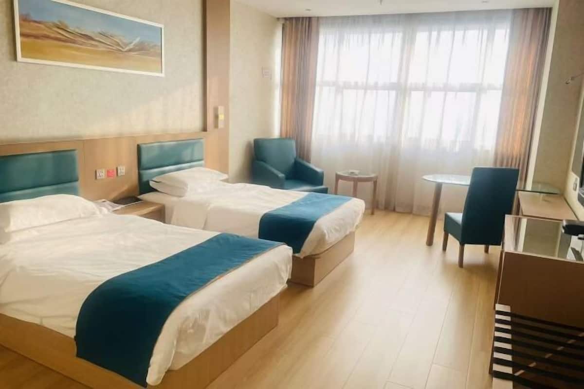 Une chambre d’hôtel avec deux lits, un bureau, une chaise, une petite table et un tableau au mur.