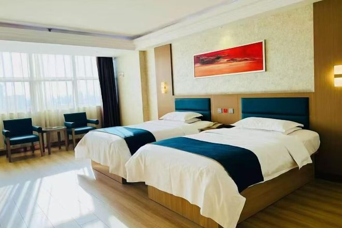 Ein Hotelzimmer mit zwei Betten, einem großen Fenster, einem Bild an der Wand und einem Schreibtisch mit Stühlen.