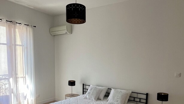 A bedroom with a large bed, two bedside tables, a hanging light fixture, and a window with curtains.