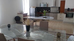 A modern kitchen with a central island, a dining area with a glass table, and a view of the living room.