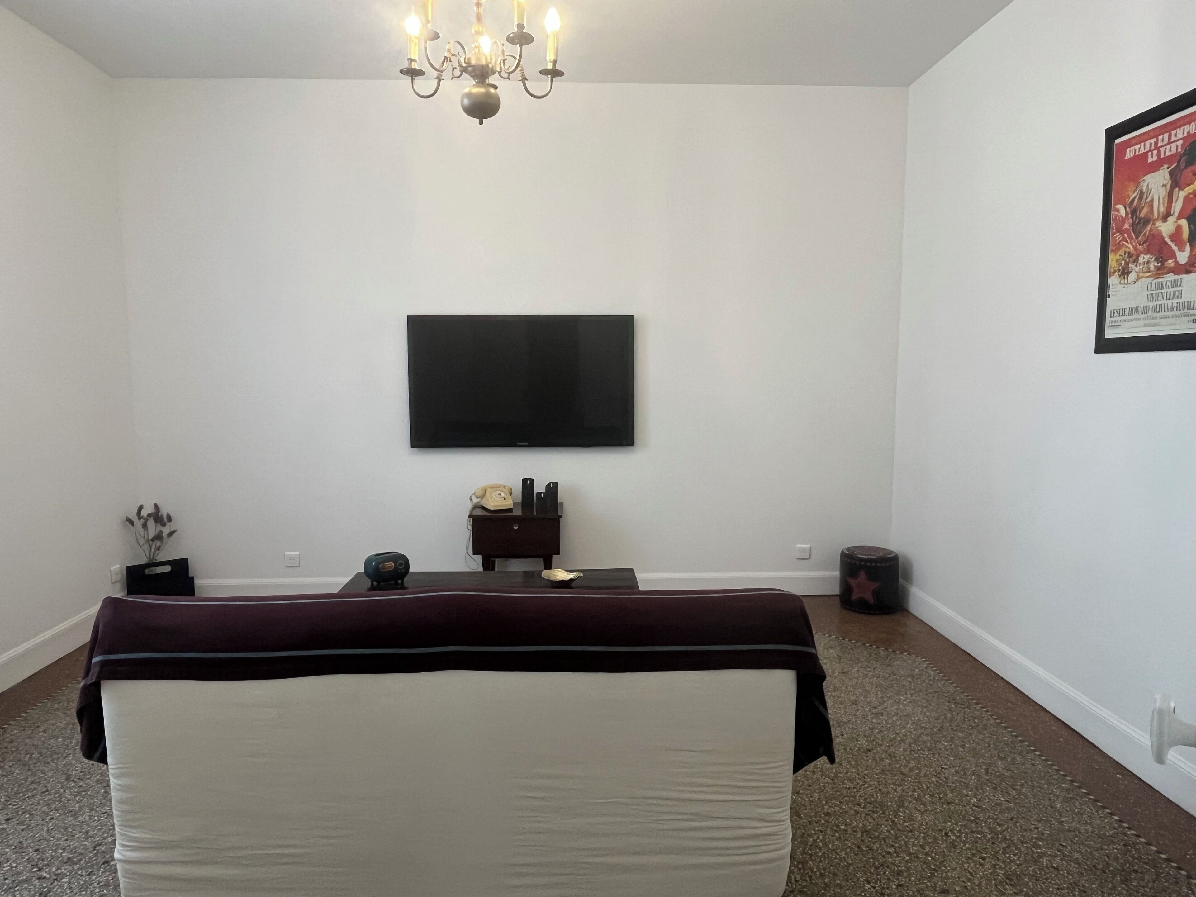 Una stanza con una TV a schermo piatto montata a parete, un tavolino con telefono e altoparlanti, un vaso decorativo e un lampadario.