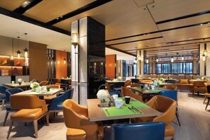 A modern restaurant with multiple dining tables and chairs, a central pillar, and a view of the city through large windows. - Hampton by Hilton Xuzhou Huaihai Road (Xuzhou)