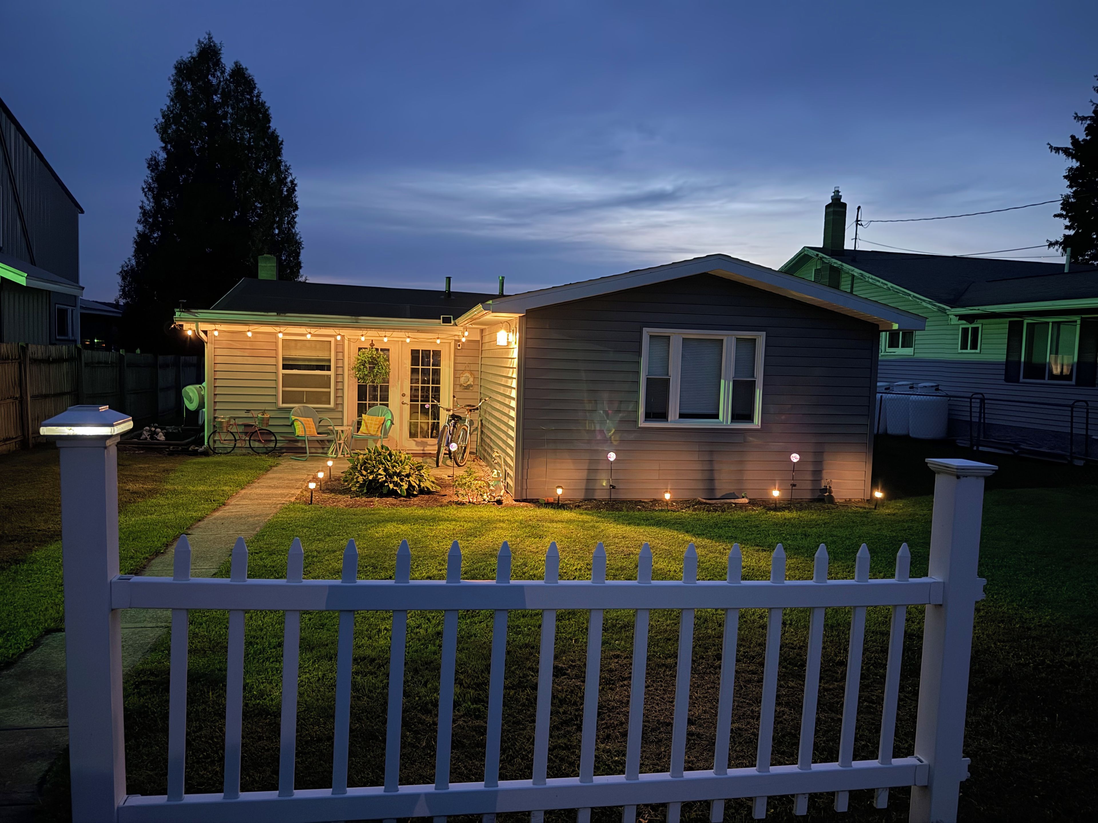 A single-story house with a porch, a small garden, and a white picket fence.