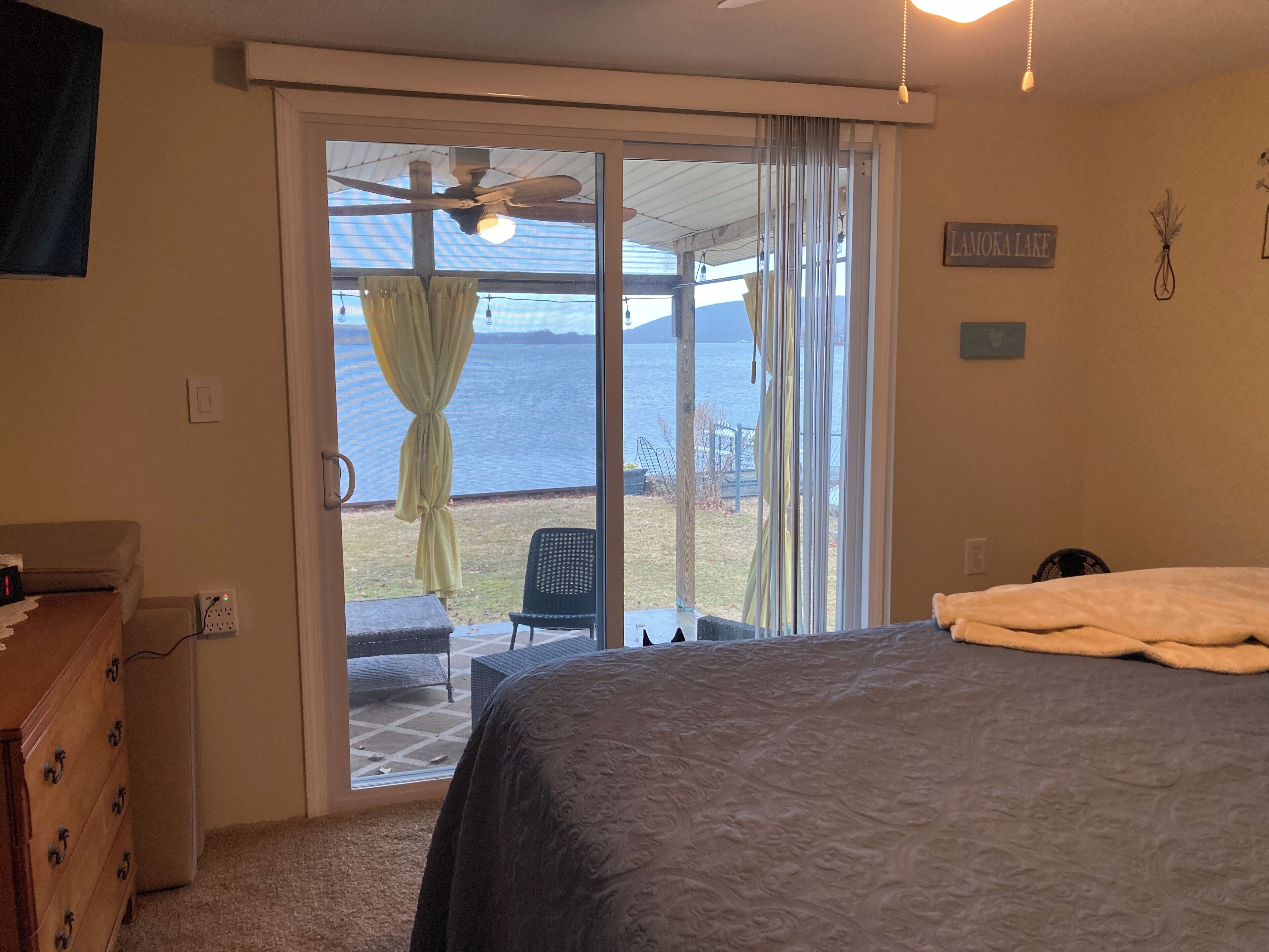Un dormitorio con cama, cómoda, ventilador de techo y vista al lago.