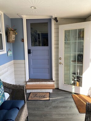 A blue door with a glass panel, a wicker chair, a cushion, a doormat, and a wooden floor.