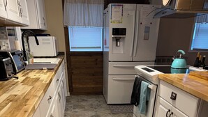 Una cocina con armarios blancos, piso con diseño de piedra, un refrigerador, una estufa y un lavamanos.