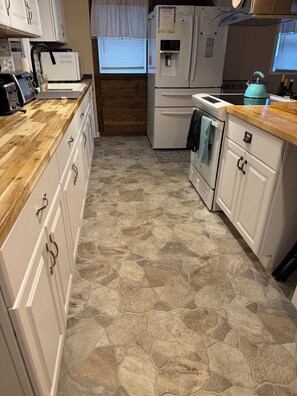 A kitchen with white cabinets, a stone-patterned floor, a refrigerator, a stove, and a sink.