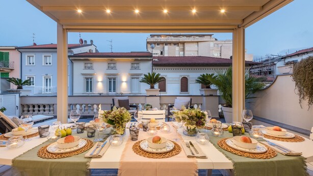 Un área de comedor al aire libre con mesas dispuestas para una comida, con vistas a un paisaje urbano de edificios y un cielo despejado.