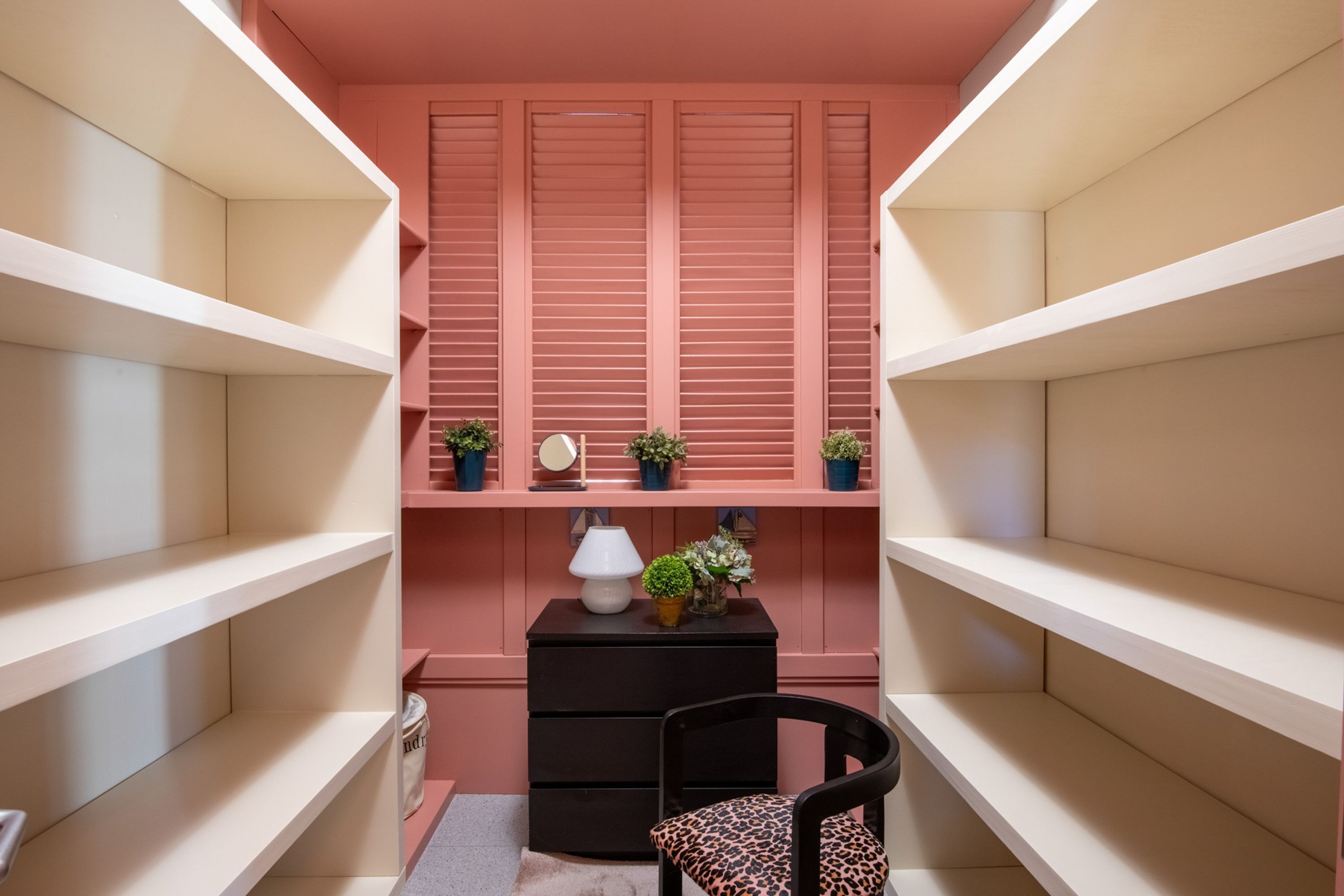 A room with pink walls, white shelves, a black dresser, a leopard print chair, and small potted plants.