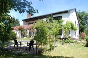 A modern house with a garden, a table, and chairs outside.