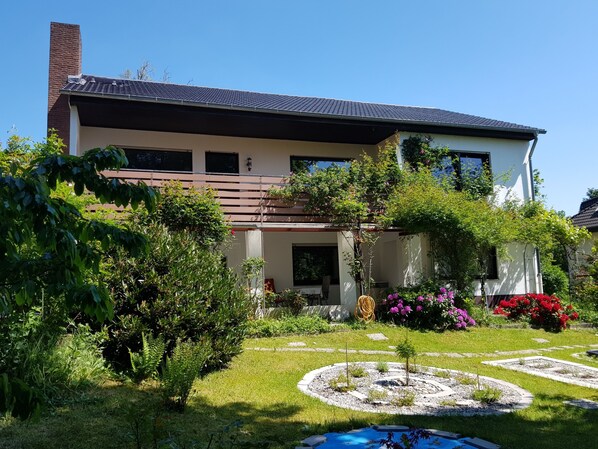 A two-story house with a garden, including a circular flower bed and a small pond.
