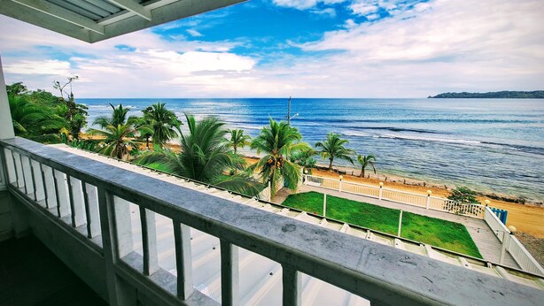 Un balcon avec vue sur l’océan et la plage, agrémenté de palmiers et offrant un ciel dégagé.