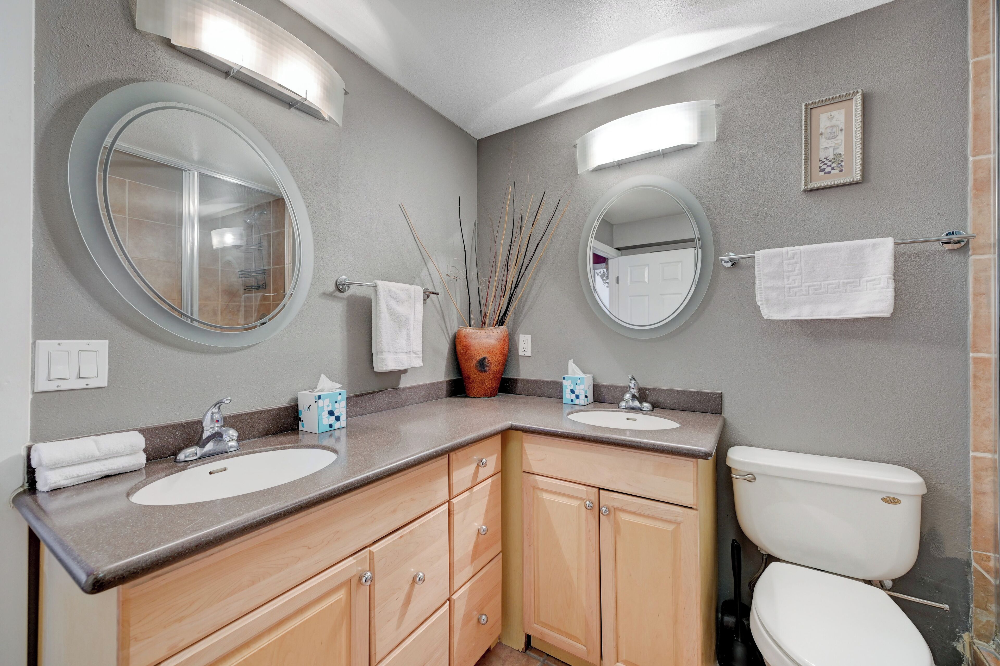 A bathroom with two sinks, a toilet, wooden cabinets, and a large mirror.