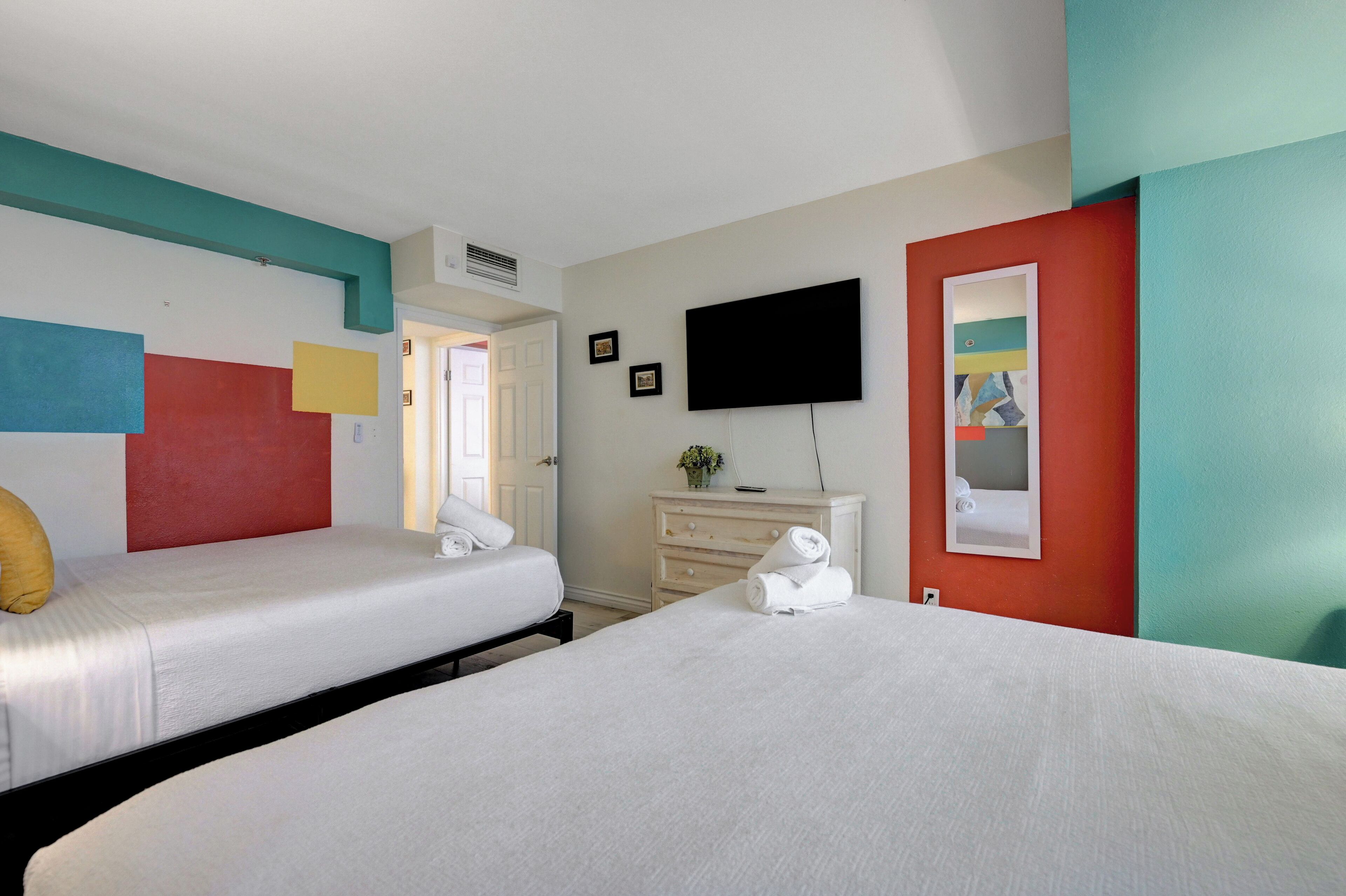 A hotel room with two beds, a TV, a dresser, and a door.