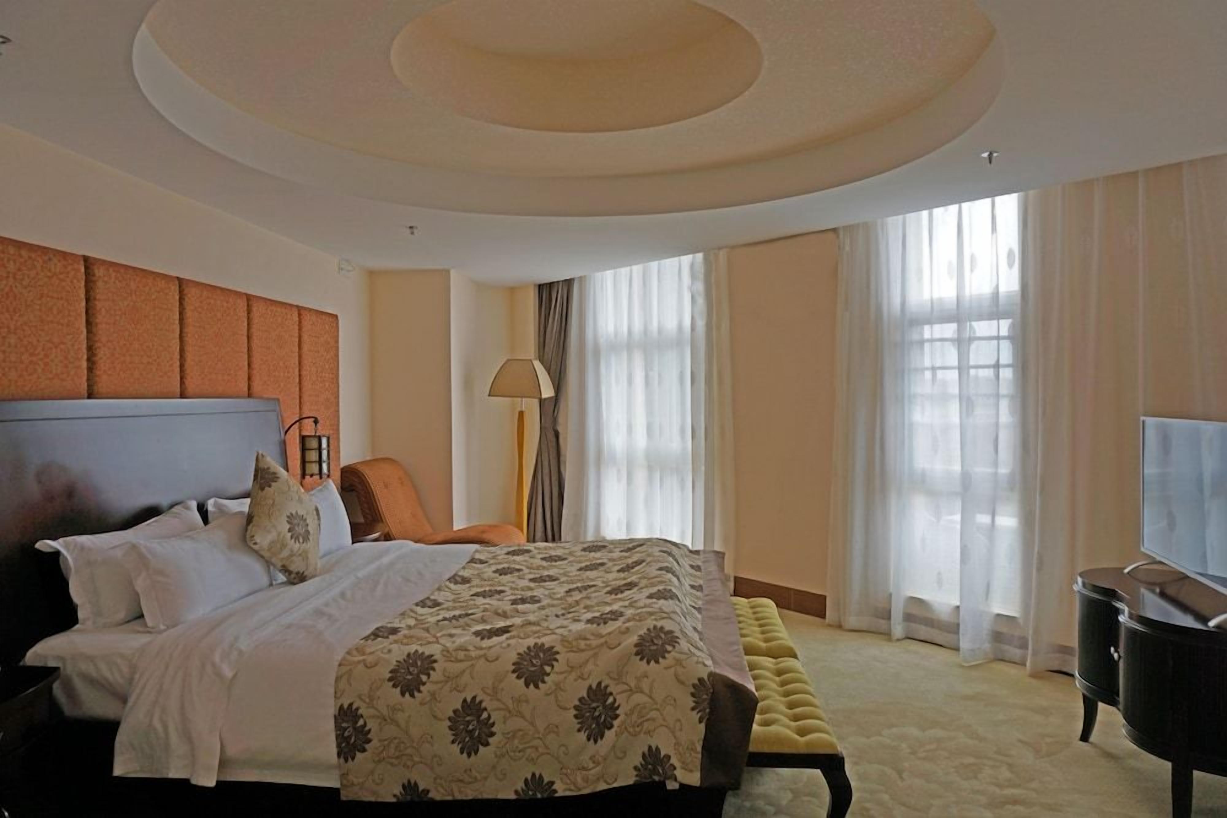 A hotel room with a large bed, a television, a sofa, and a lamp.