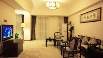 Habitación de hotel con televisión, sofá, mesa, lámpara y planta decorativa.
