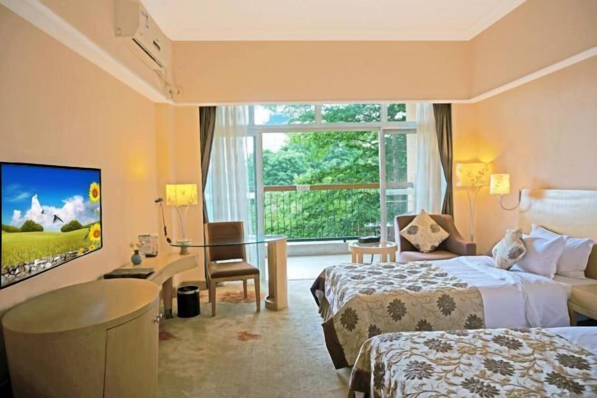 Ein Hotelzimmer mit Bett, Schreibtisch mit Stuhl, Fernseher und Fenster mit Blick auf Grünflächen.