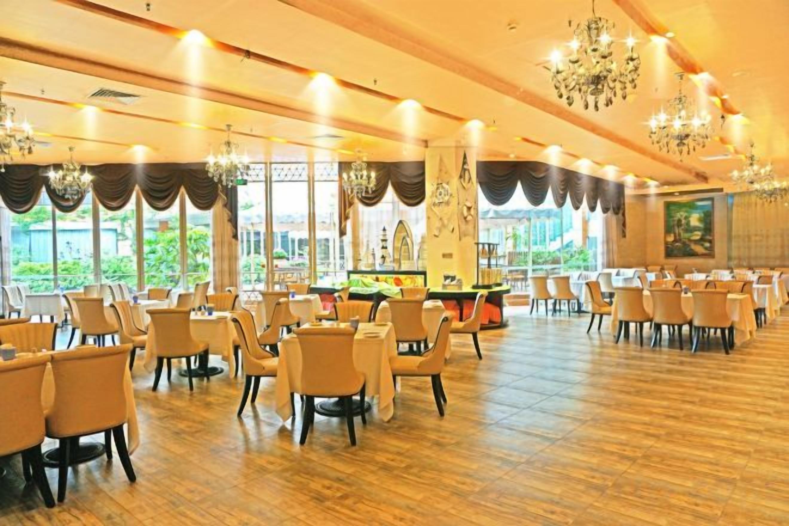 Un amplio salón de banquetes con filas de mesas y sillas, ventanas grandes y candelabros.