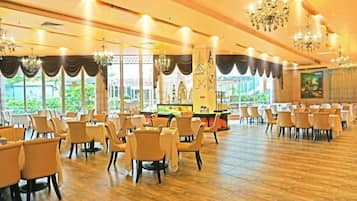 Un amplio salón de banquetes con filas de mesas y sillas, ventanas grandes y candelabros.