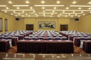 Un salón de conferencias con varias mesas y sillas dispuestas en filas, con un cuadro grande en la pared y obras de arte enmarcadas a un lado.