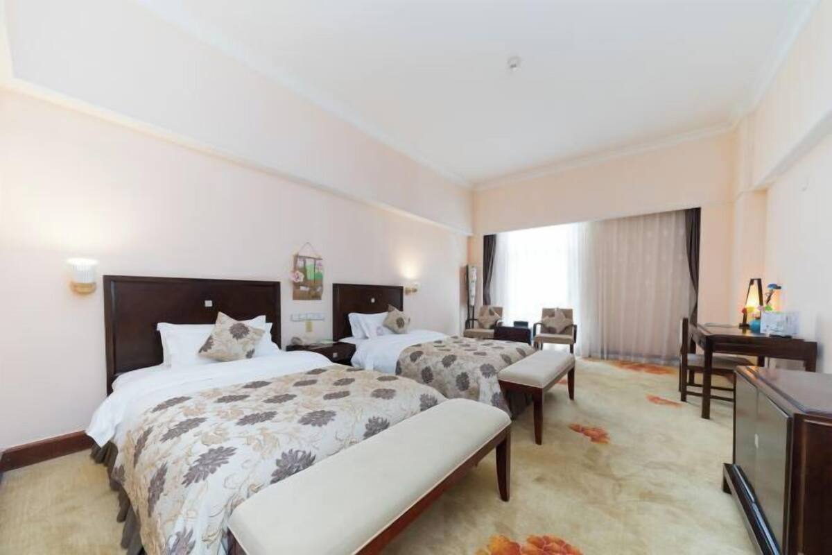 Ein Hotelzimmer mit zwei Betten, einem Schreibtisch, einem Sessel und einem Fernseher.