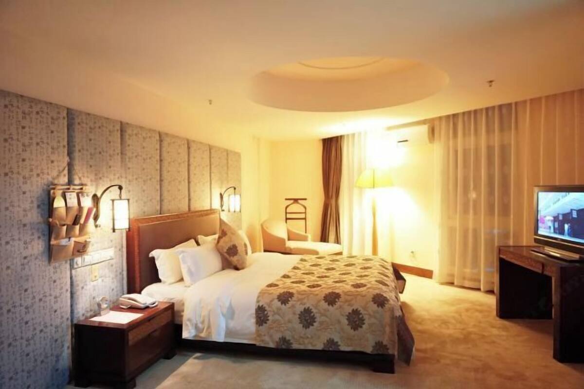 Ein Hotelzimmer mit einem großen Bett, einem Nachttisch mit Lampe, einem Fernseher und einem Wandregal mit Dekoration.