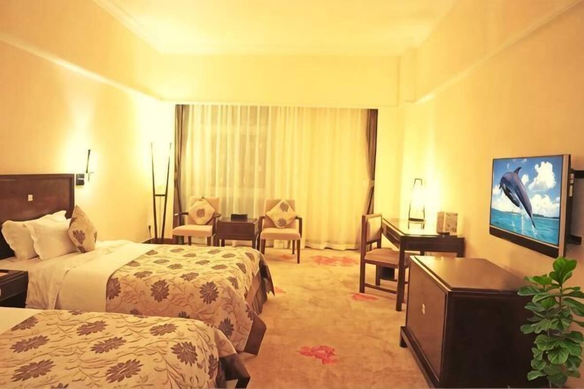 Ein Hotelzimmer mit zwei Betten, einem Schreibtisch, einem Sessel, einem Fernseher und einem großen Fenster mit Vorhängen.