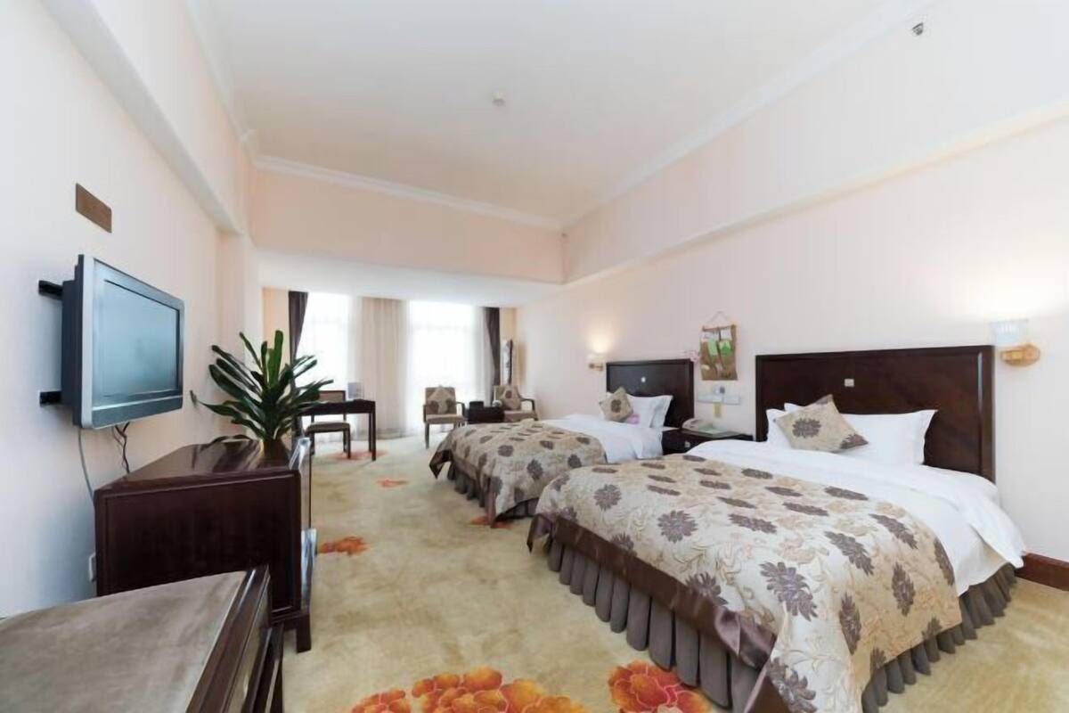 Ein Hotelzimmer mit zwei Betten, einem Fernseher, einem Schreibtisch und einem Sessel.